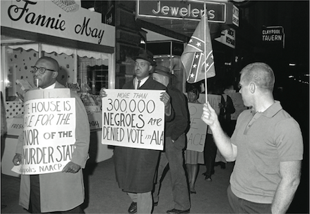 A man held a Confederate flag as demonstrators, including one with a sign saying "More than 300,000 Negroes Are Denied Vote in Ala," marched in front of an Indianapolis hotel where George Wallace, the governor of Alabama, was staying in April 1964. Credit Bob Daugherty/ Associated Press
